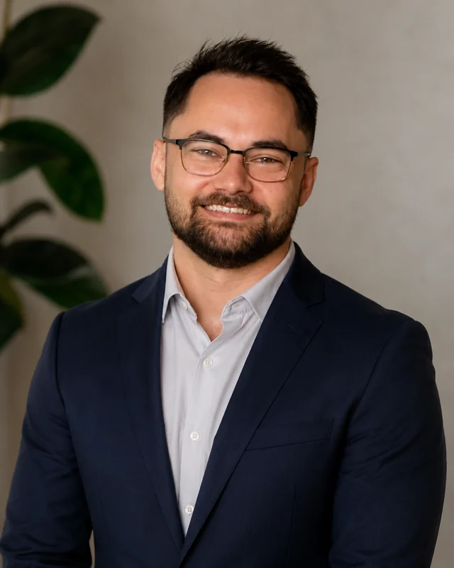 Daniel, smiling, wearing glasses and a navy suit jacket.